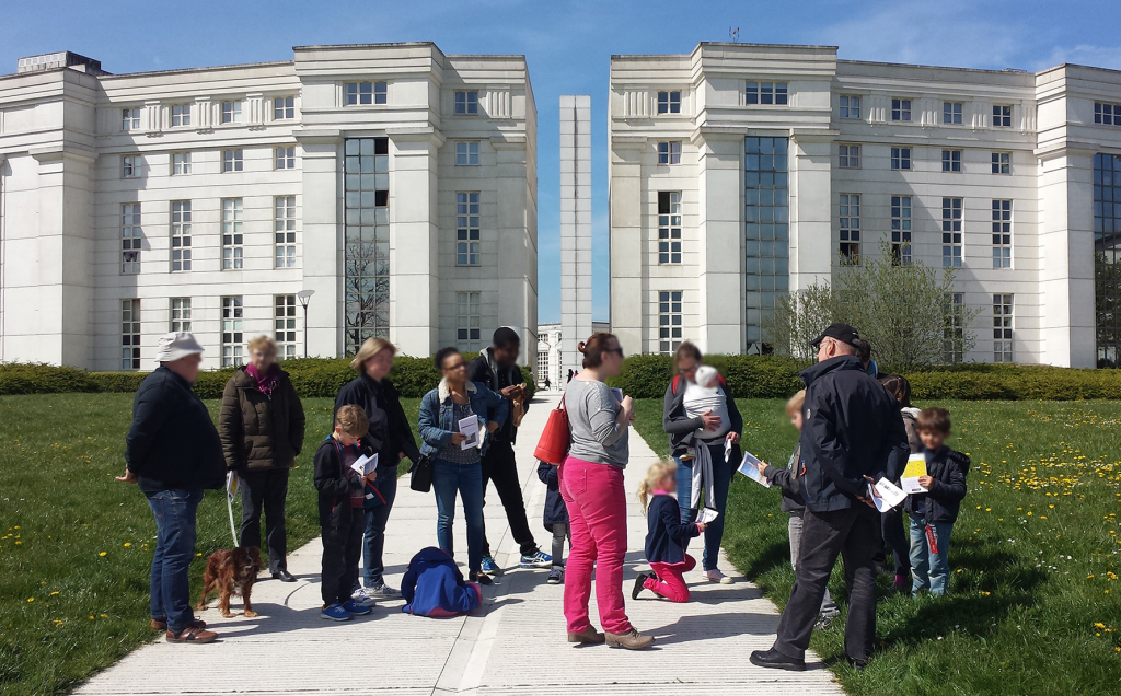 Groupe d'enfant et d'adultes devant la Tour Belvédère en train de participer à une enquête ludique à l'Axe Majeur organisée par l'office de tourisme de CERGY-PONTOISE